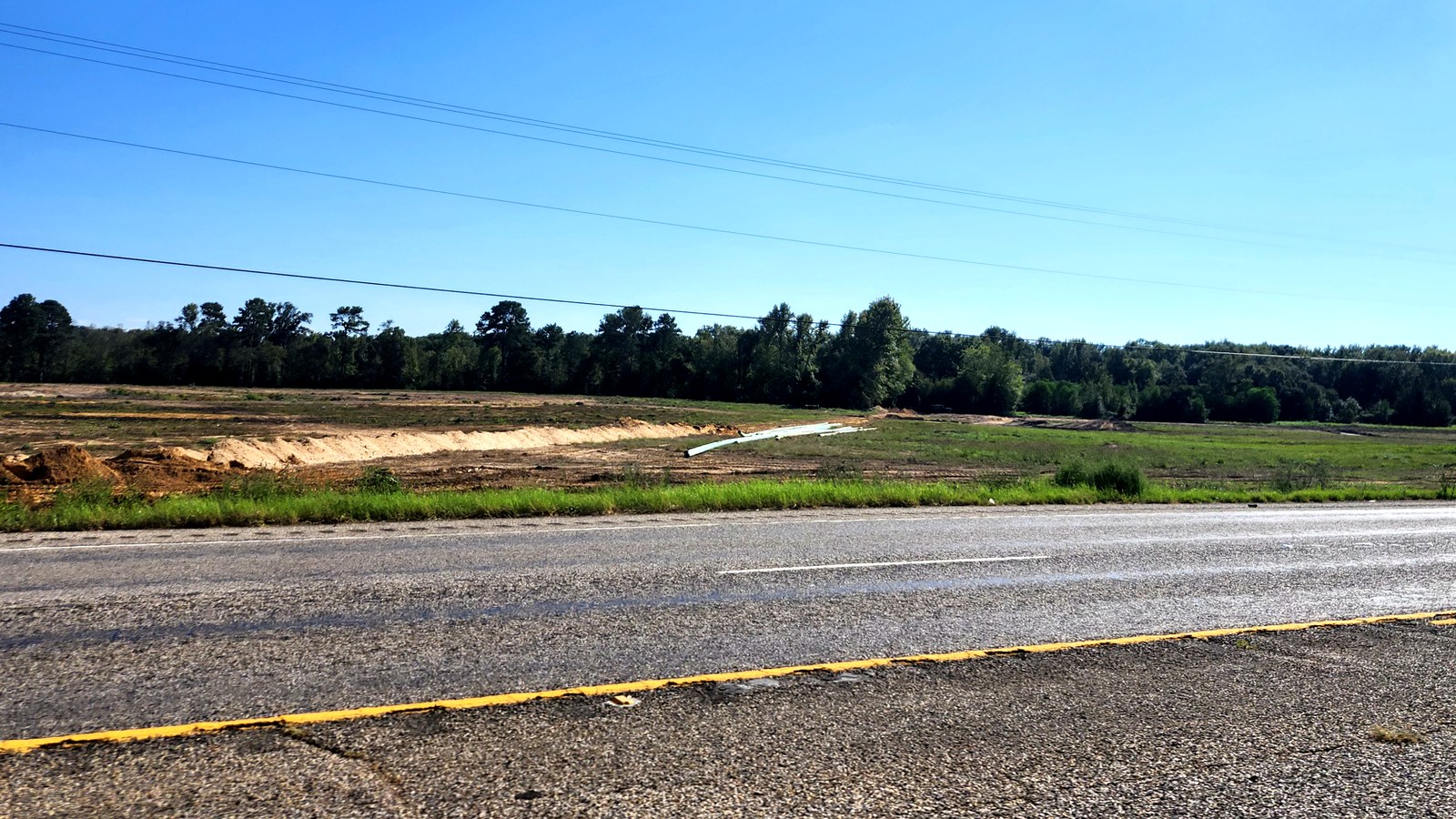 A long sand berm and a green drainage pipe in a cleared field below a tree line, seen from Hwy 31 in Chandler
