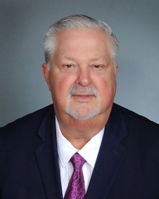 Portrait of Rick Ford in a navy suit, white shirt and pink patterned tie