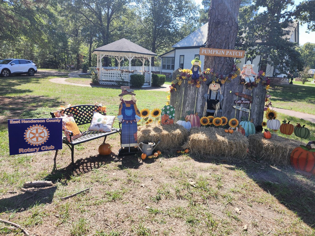 A fall lawn display with pumpkins and hay bales, gazebo behind