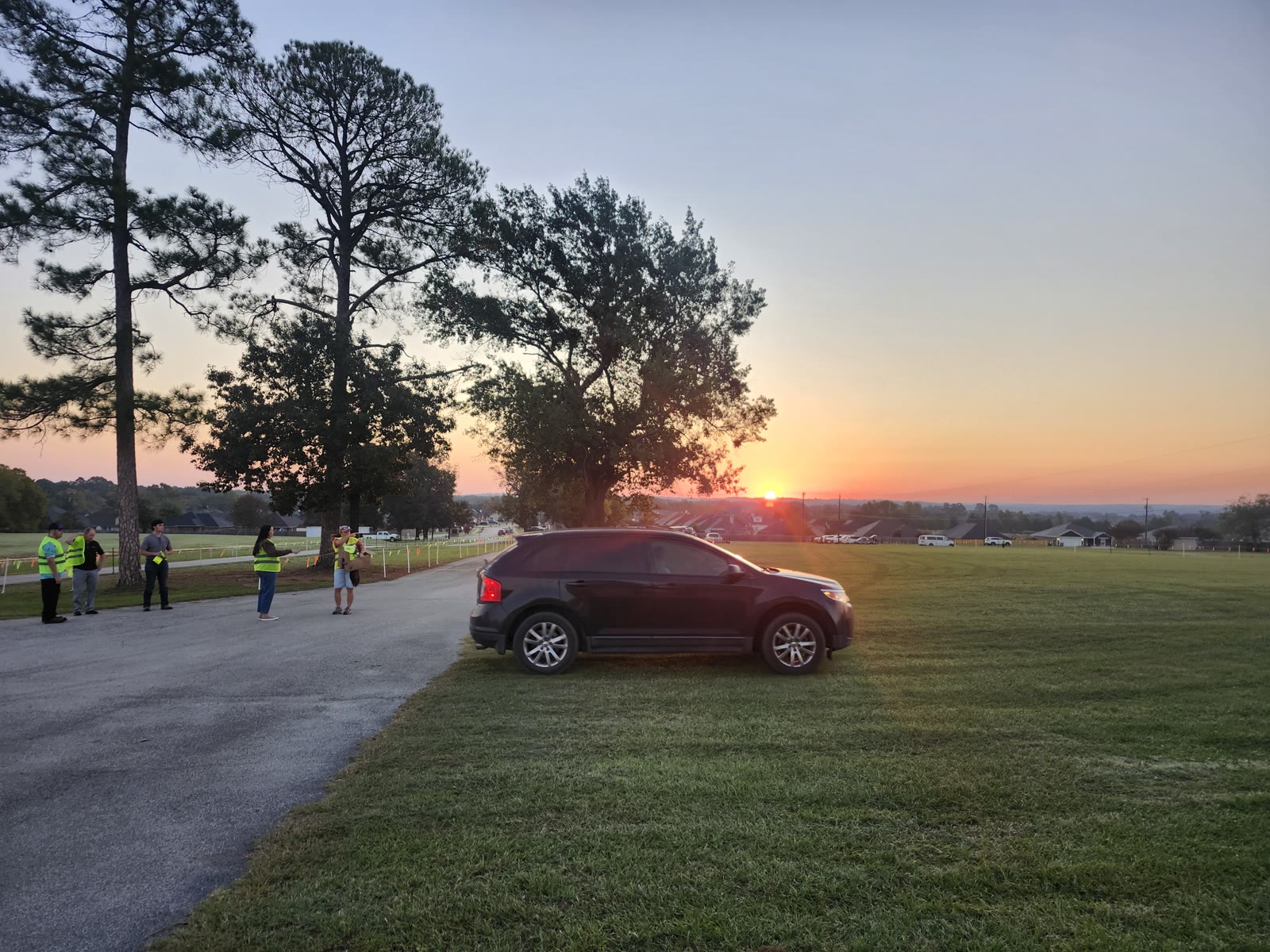 Volunteers in yellow safety vests greet early arrivals at Winchester Park at sunrise