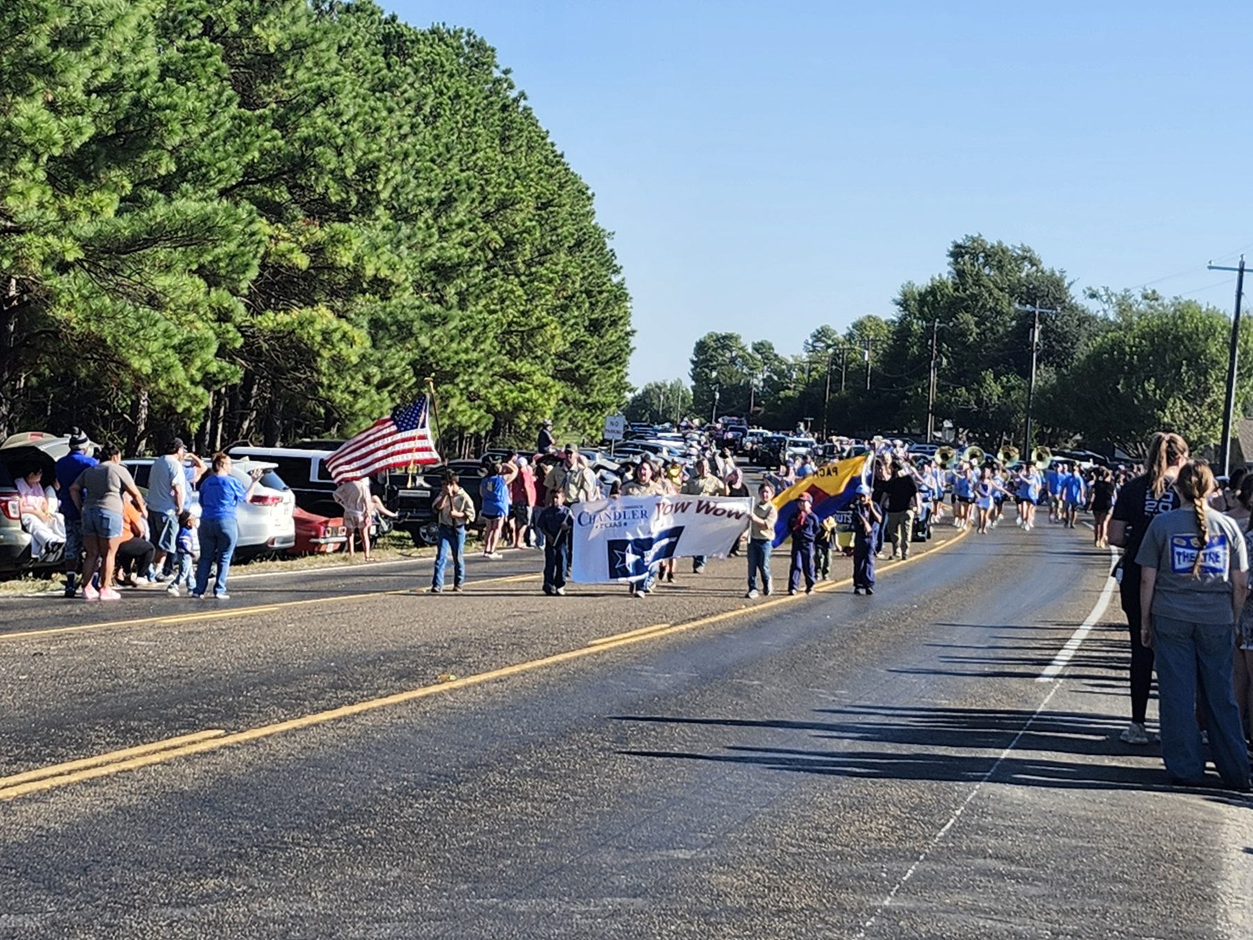 Cub Scouts carry the Chandler Pow Wow banner and the American flag down the road as spectators watch and the band follows