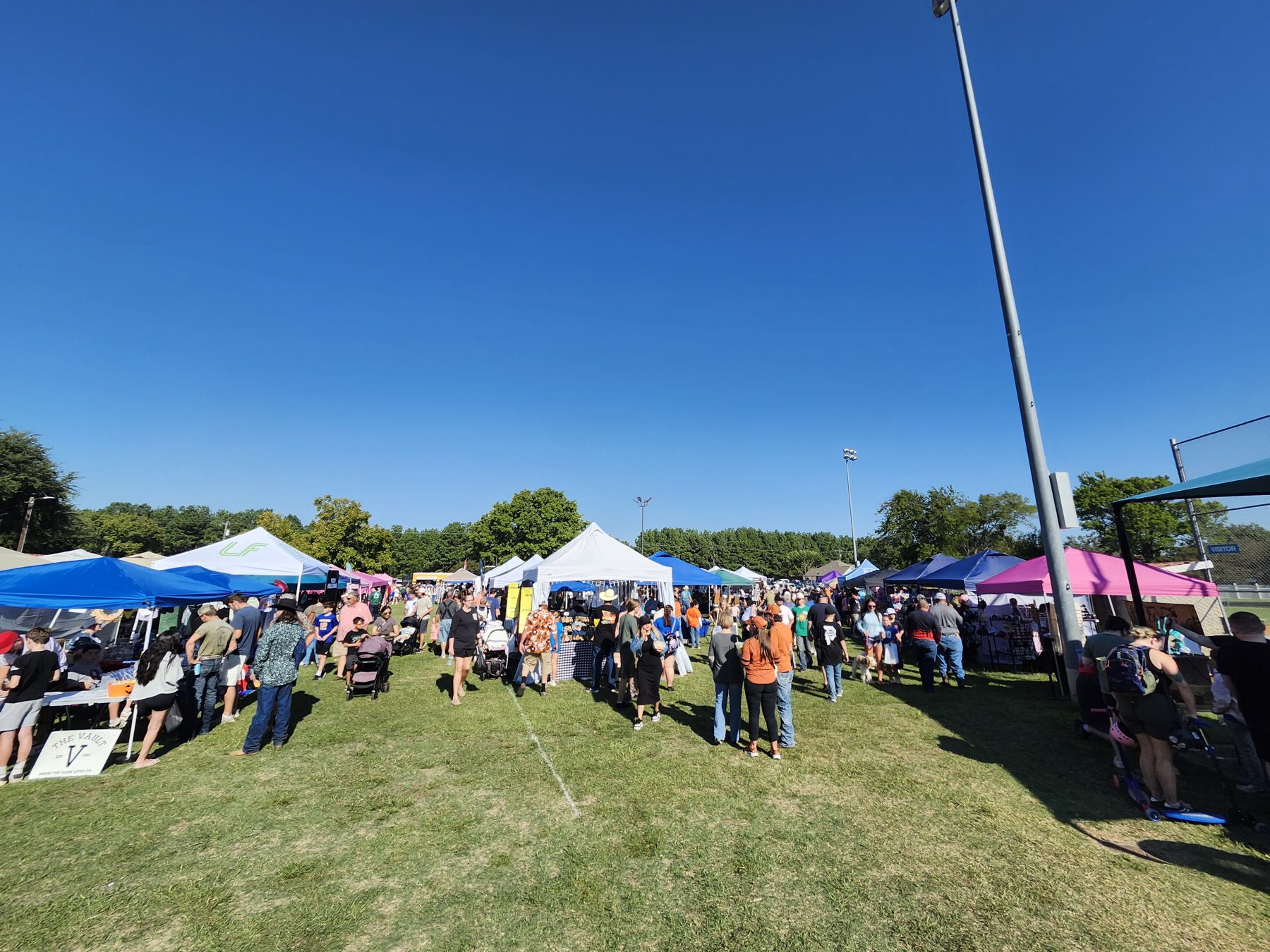 Crowds fill the grassy rows between vendor tents at Winchester Park under a clear blue sky