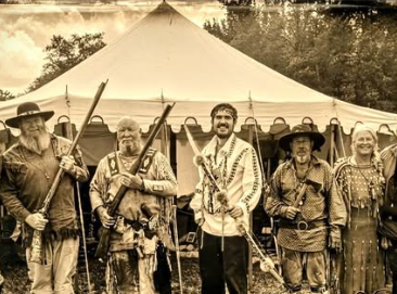 Pioneer Day 2026 reenactors in frontier dress holding long rifles in front of a white tent