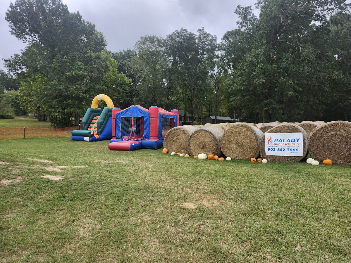 Inflatables and a row of round hay bales trimmed with pumpkins sit along the edge of the field
