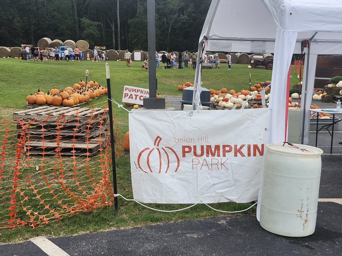 The Union Hill Pumpkin Park banner welcomes guests beside the pumpkin patch, with the hay bale area busy in the background